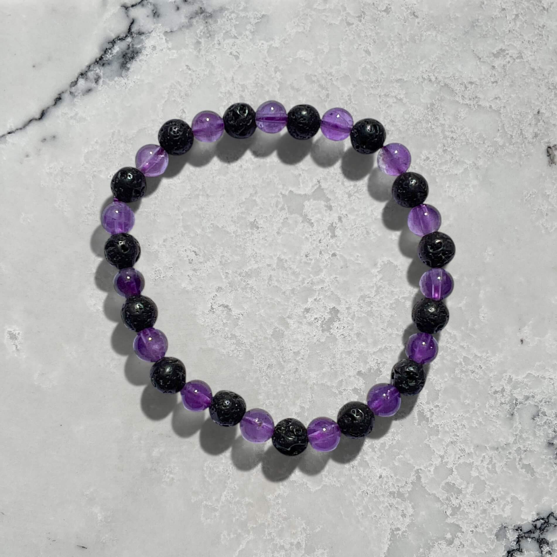 Black lava and purple amethyst crystal bead bracelet on a marble surface