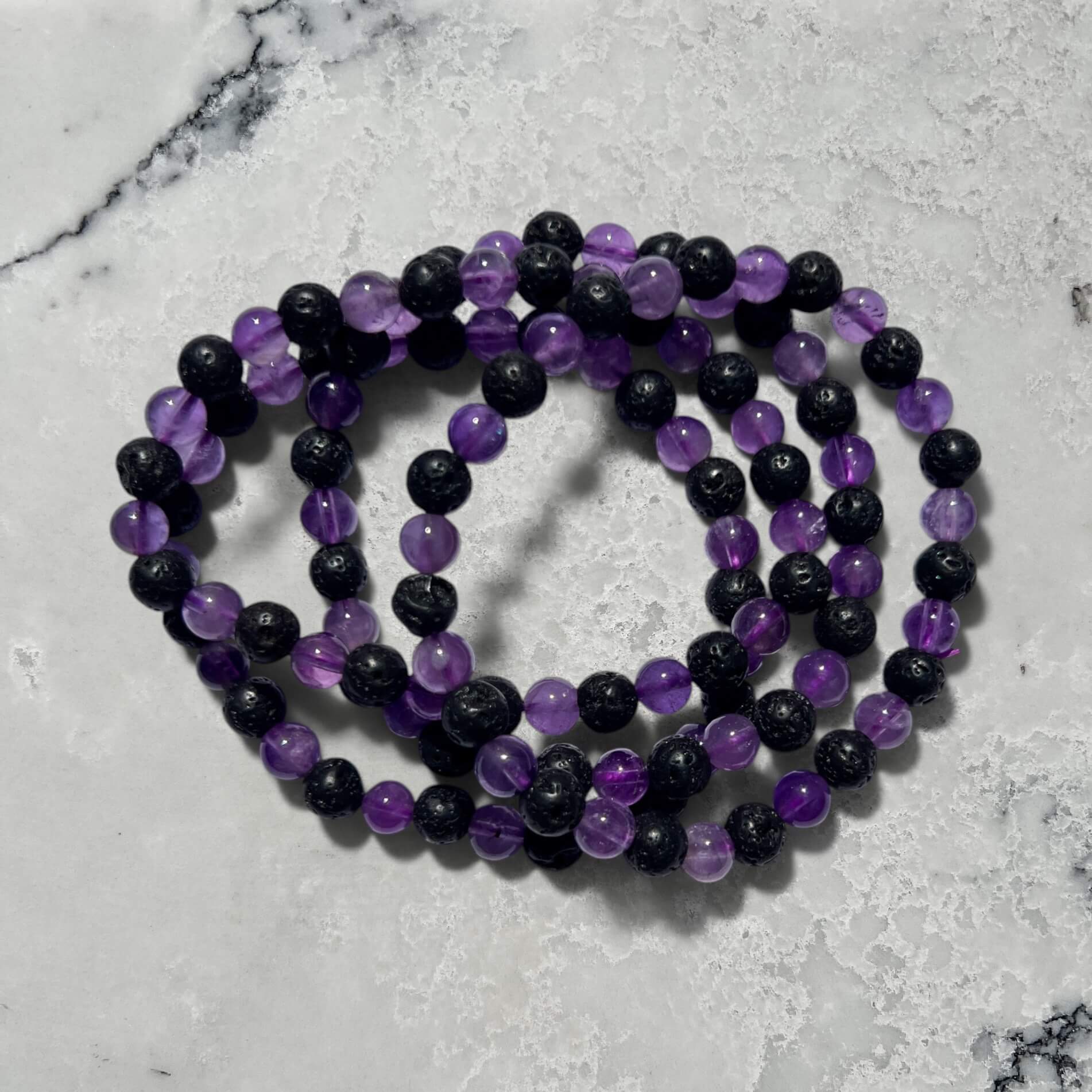 Stack of black lave and purple amethyst crystal bead bracelets on a marble surface