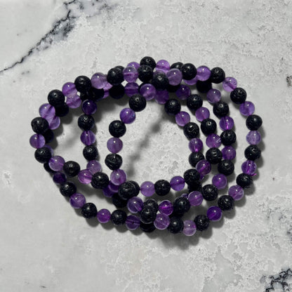Stack of black lave and purple amethyst crystal bead bracelets on a marble surface