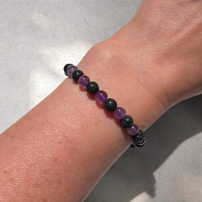 Black lava and purple amethyst crystal bead bracelet on a wrist against a neutral background