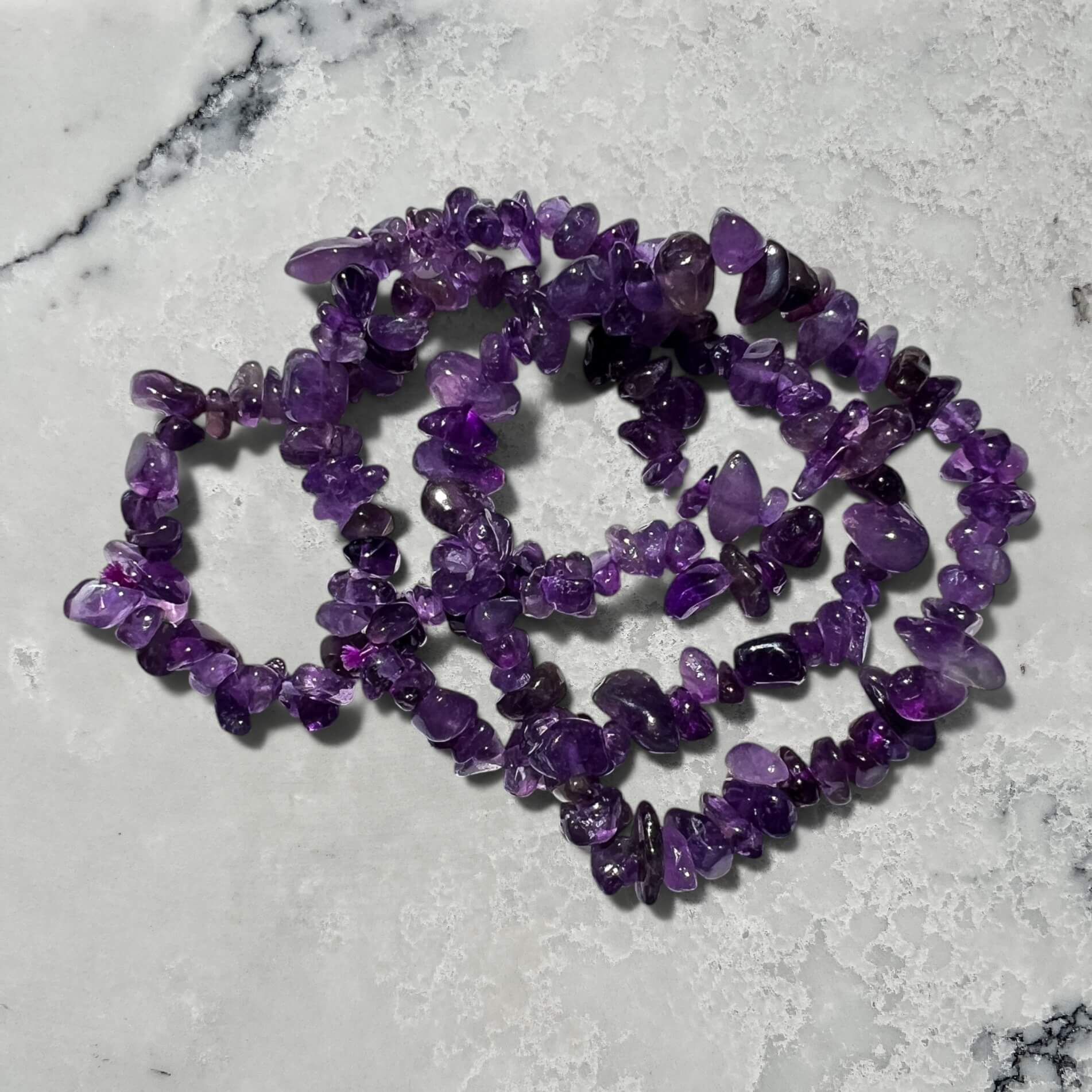 Stack of Purple amethyst crystal chip bracelets on a marble surface