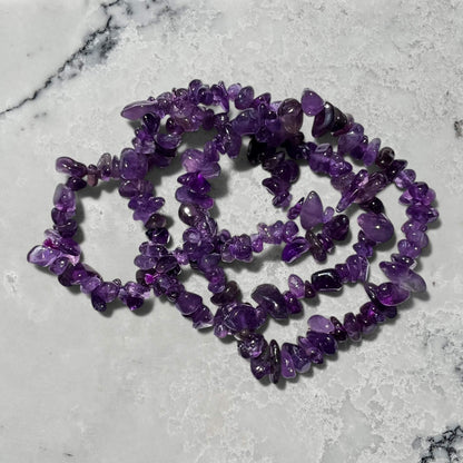 Stack of Purple amethyst crystal chip bracelets on a marble surface