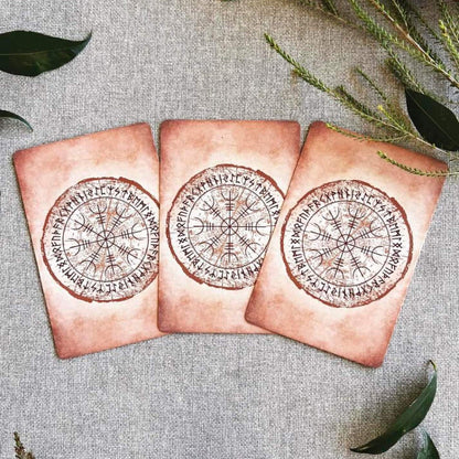 Three decorative oracle card backs with compass designs on a textured surface with leaves.
