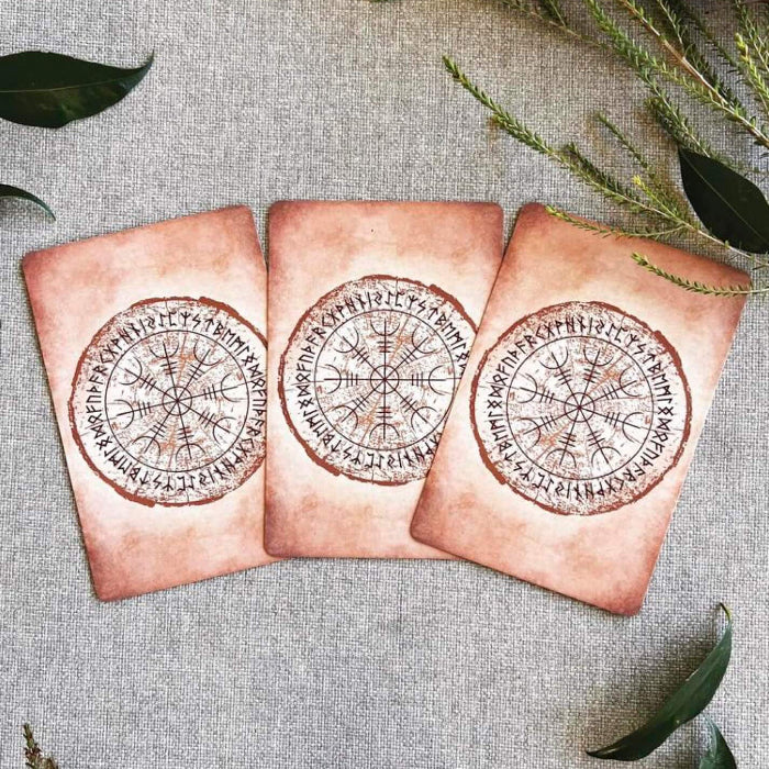 Three decorative oracle card backs with compass designs on a textured surface with leaves.
