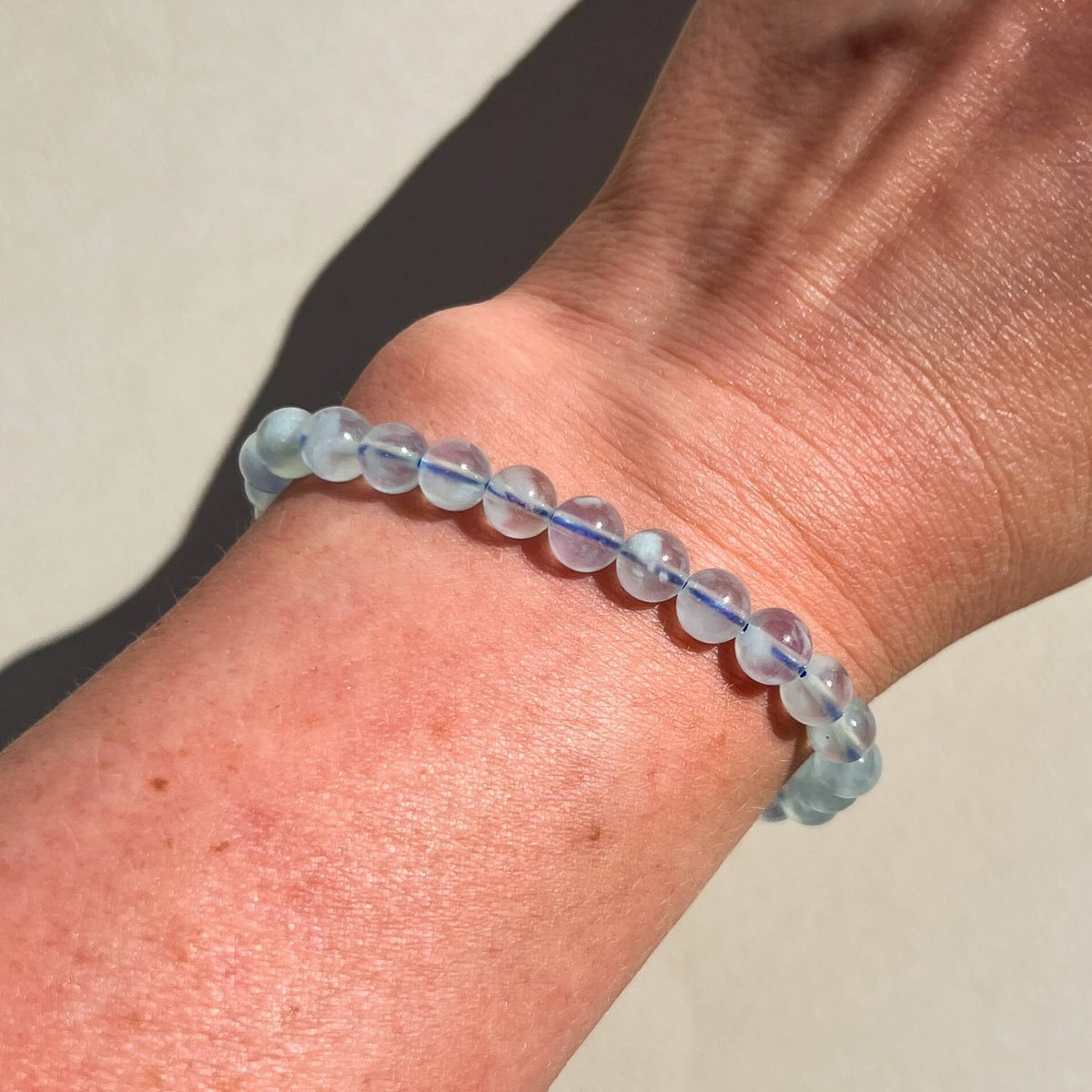 A close-up of a person's wrist wearing a beaded bracelet made of light blue Aquamarine gem, semi-opaque round beads.