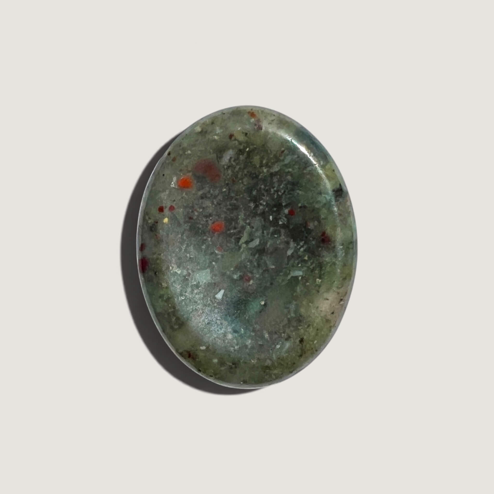 A polished oval bloodstone worry stone featuring a mottled pattern of dark green, light olive green and small red inclusions, displayed on a neutral light grey background.