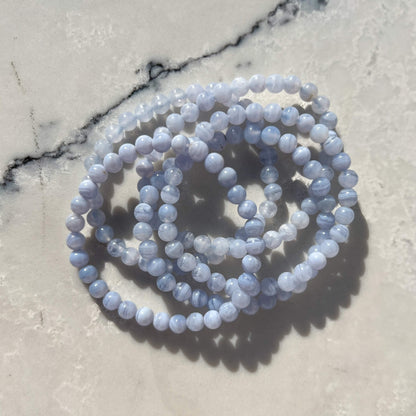 Stack of multiple Blue Lace Agate crystal bead bracelets on a grey and white marble surface