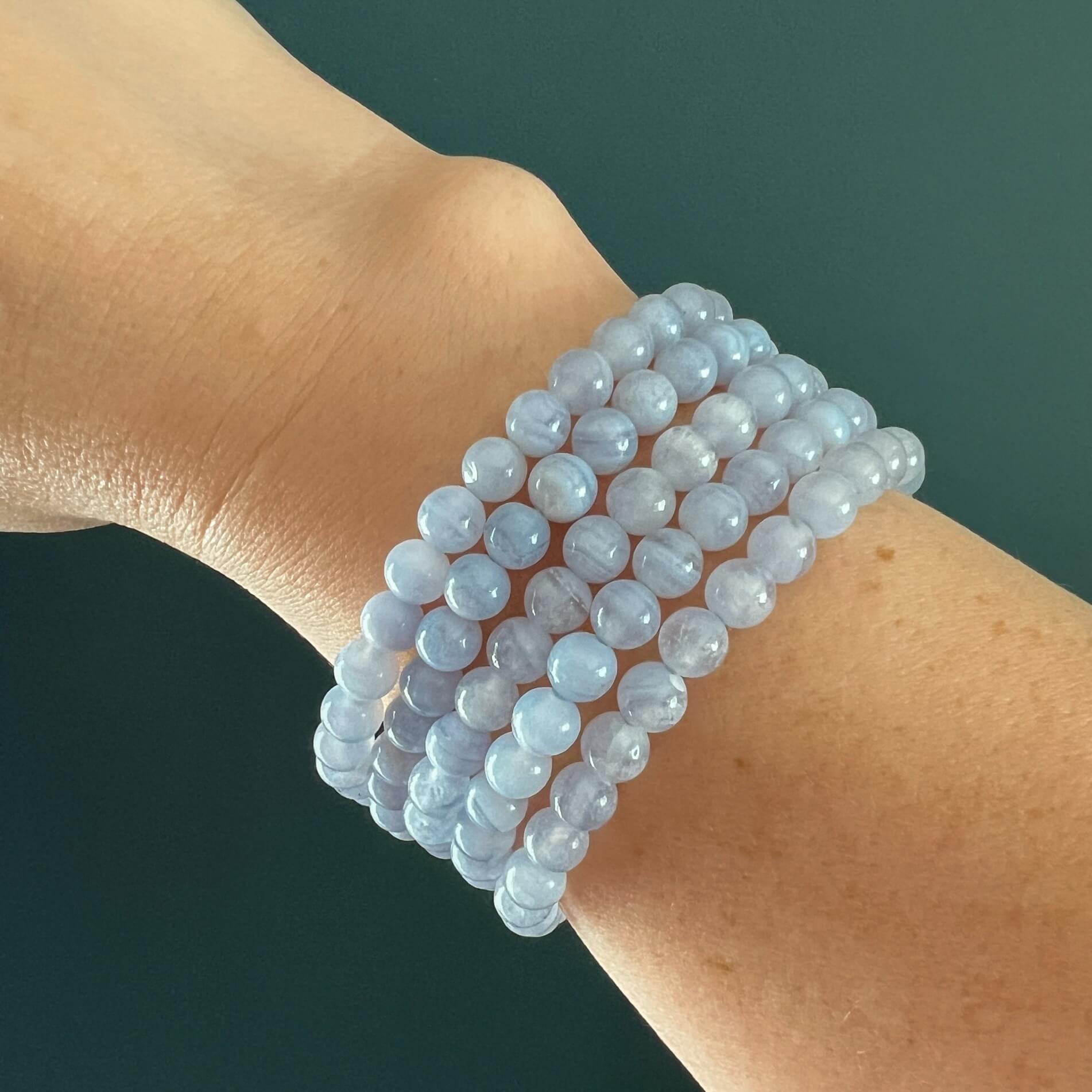Stack of Blue Lace Agate crystal bead bracelets on a woman's wrist against a dark teal background