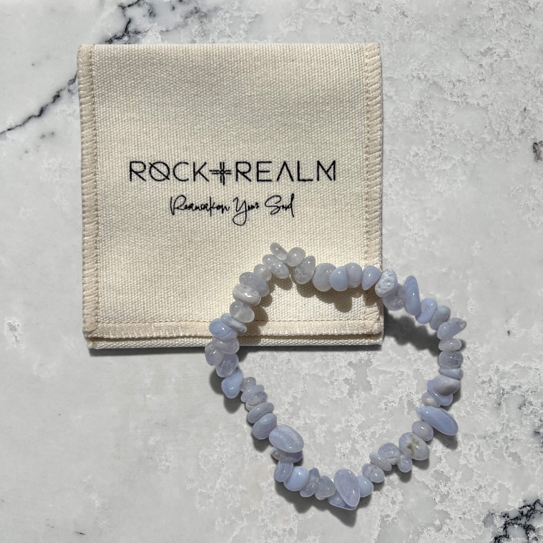 Blue Agate crystal chip gemstone bracelet on a marble surface with cream cotton 'Rock + Realm' pouch.