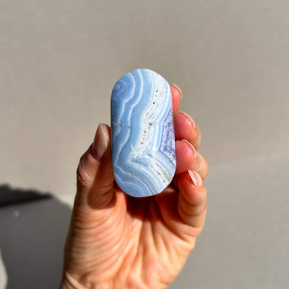 A intricately banded blue. lace agate oval palm stone held to camera for a close up