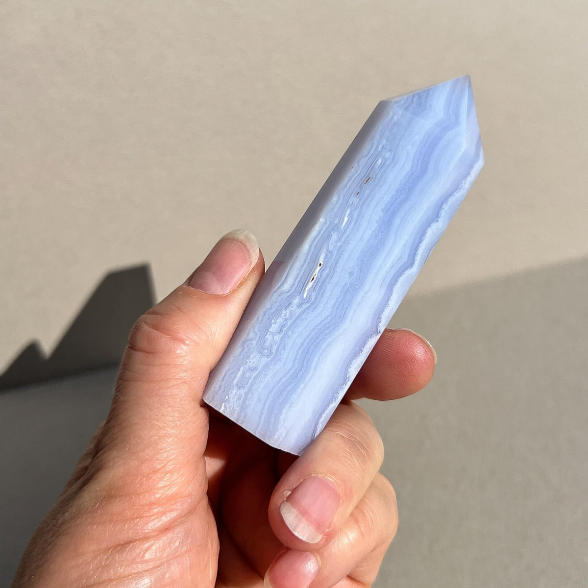 A hand holding a polished light blue lace agate crystal point against a neutral beige background.
