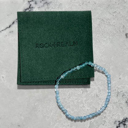 Blue Topaz gemstone bead bracelet on a green jewellery pouch with 'Rock + Realm' branding on a marble surface