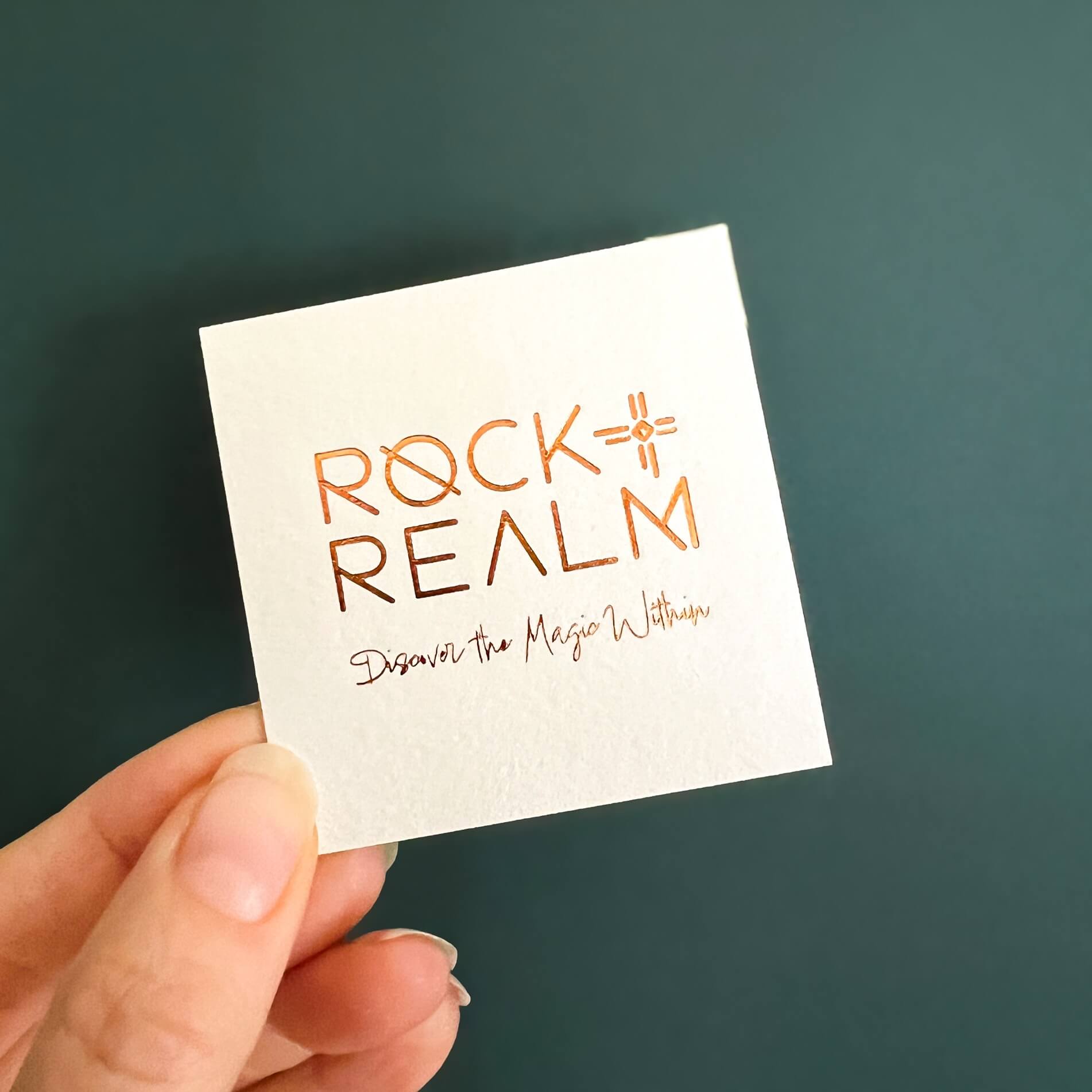 'Rock + Realm' branded lux card with copper foil text against a dark teal backdrop