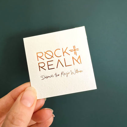 'Rock + Realm' branded lux card with copper foil text against a dark teal backdrop