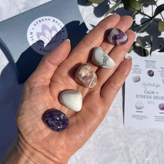 white scolecite, chevron amethyst, peach moonstone, purple lepidolite and white Howlite crystal tumble stones on an open palm