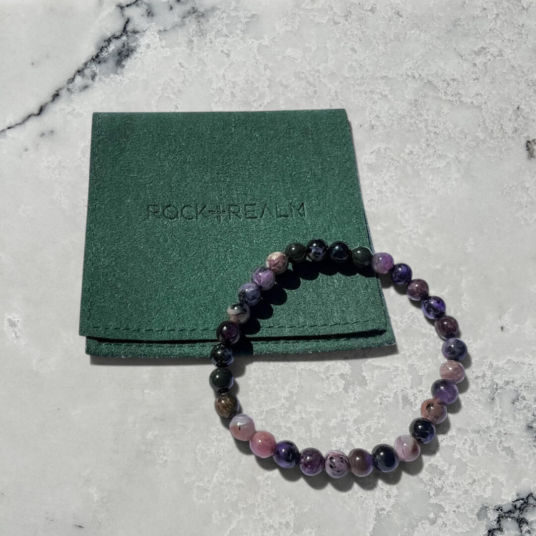 Black, Purple, grey & pink Chaorite crystal bead bracelet on a white surface with a green pouch labeled 'Rock + Realm' in the background.
