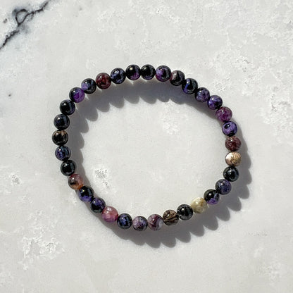 Purple, lilac and black Chaorite crystal bead bracelet on a light grey and white marble surface