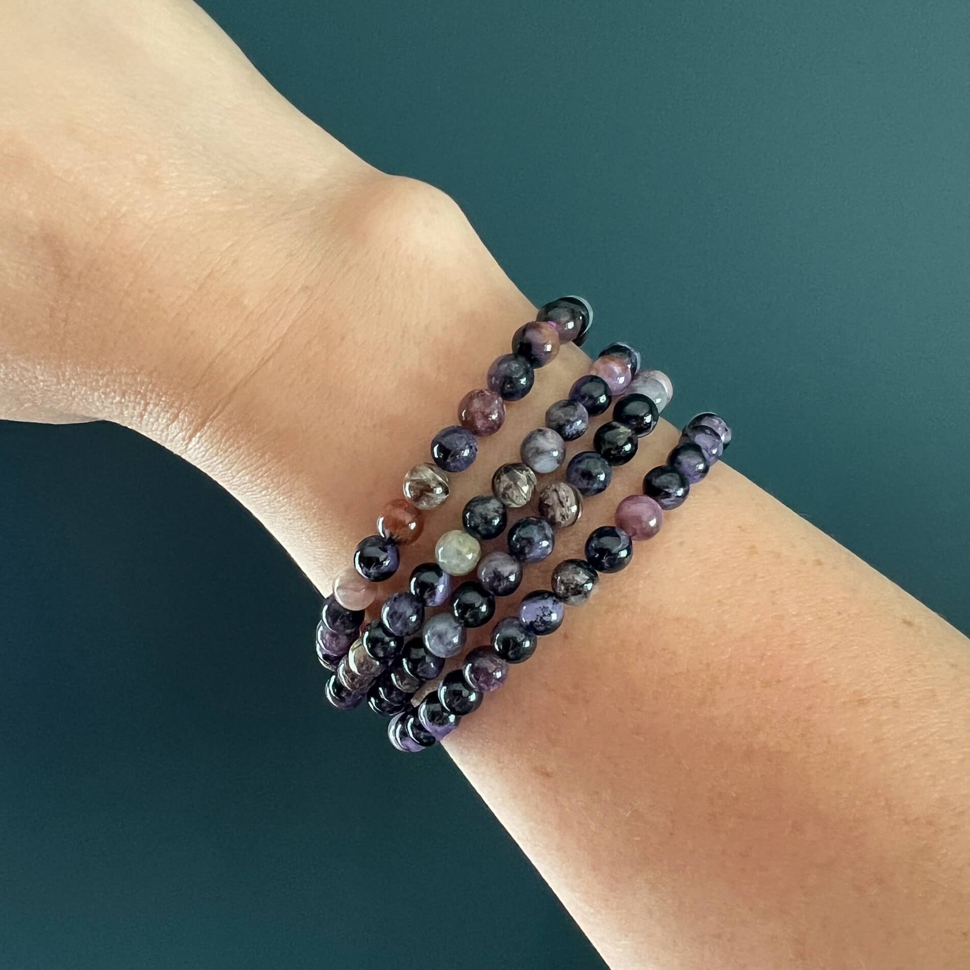 Purple, lilac and black Chaorite crystal bead bracelet stack on a woman's wrist with a dark teal backdrop