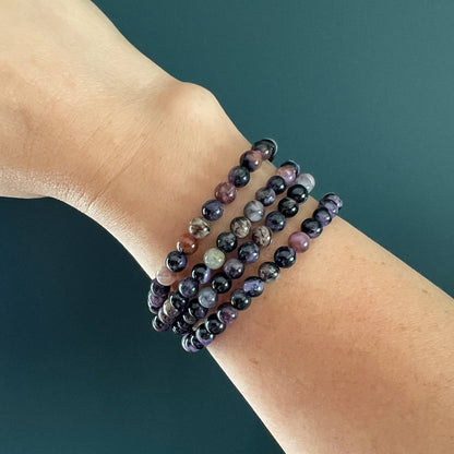 Purple, lilac and black Chaorite crystal bead bracelet stack on a woman's wrist with a dark teal backdrop
