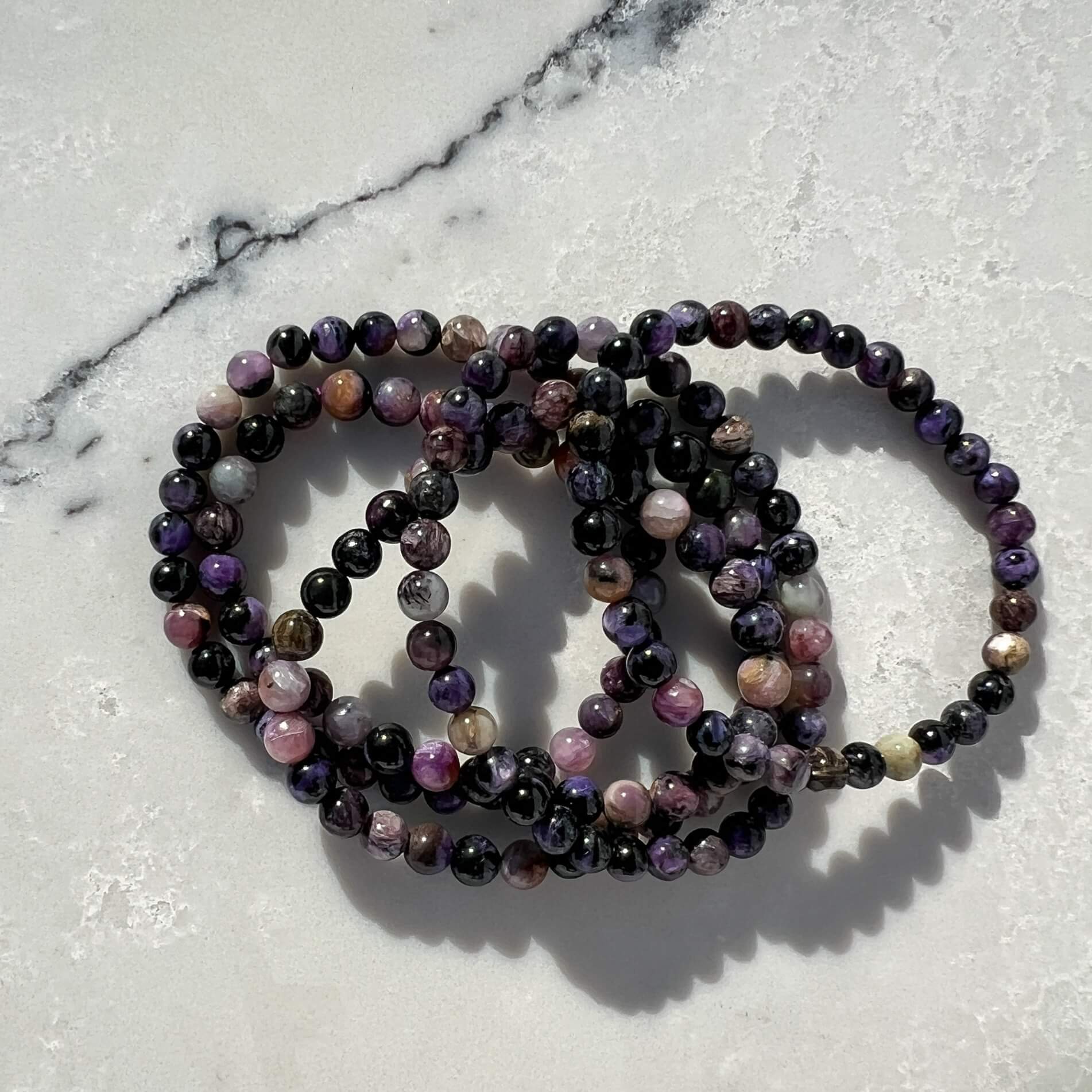 Stack of five Purple, lilac and black Chaorite crystal bead bracelets on a white and grey marble surface