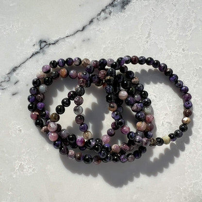 Stack of five Purple, lilac and black Chaorite crystal bead bracelets on a white and grey marble surface