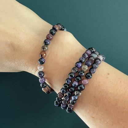 Purple, lilac and black Chaorite crystal bead bracelet stack on a woman's wrist with a teal background