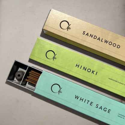 Three incense boxes from the brand Chie, arranged diagonally on a light grey surface. The boxes are light beige (Sandalwood), light green (Hinoki), and light aqua (White Sage).