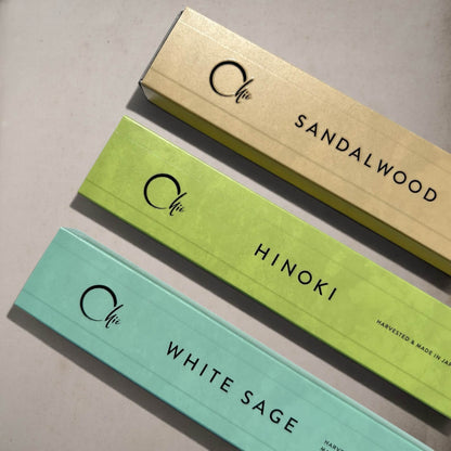 Three long rectangular product boxes arranged diagonally on a light neutral surface. The boxes are labeled with the brand name 'Chie' and scent names 'SANDALWOOD', 'HINOKI', and 'WHITE SAGE', with colours corresponding to sandalwood, hinoki and white sage.