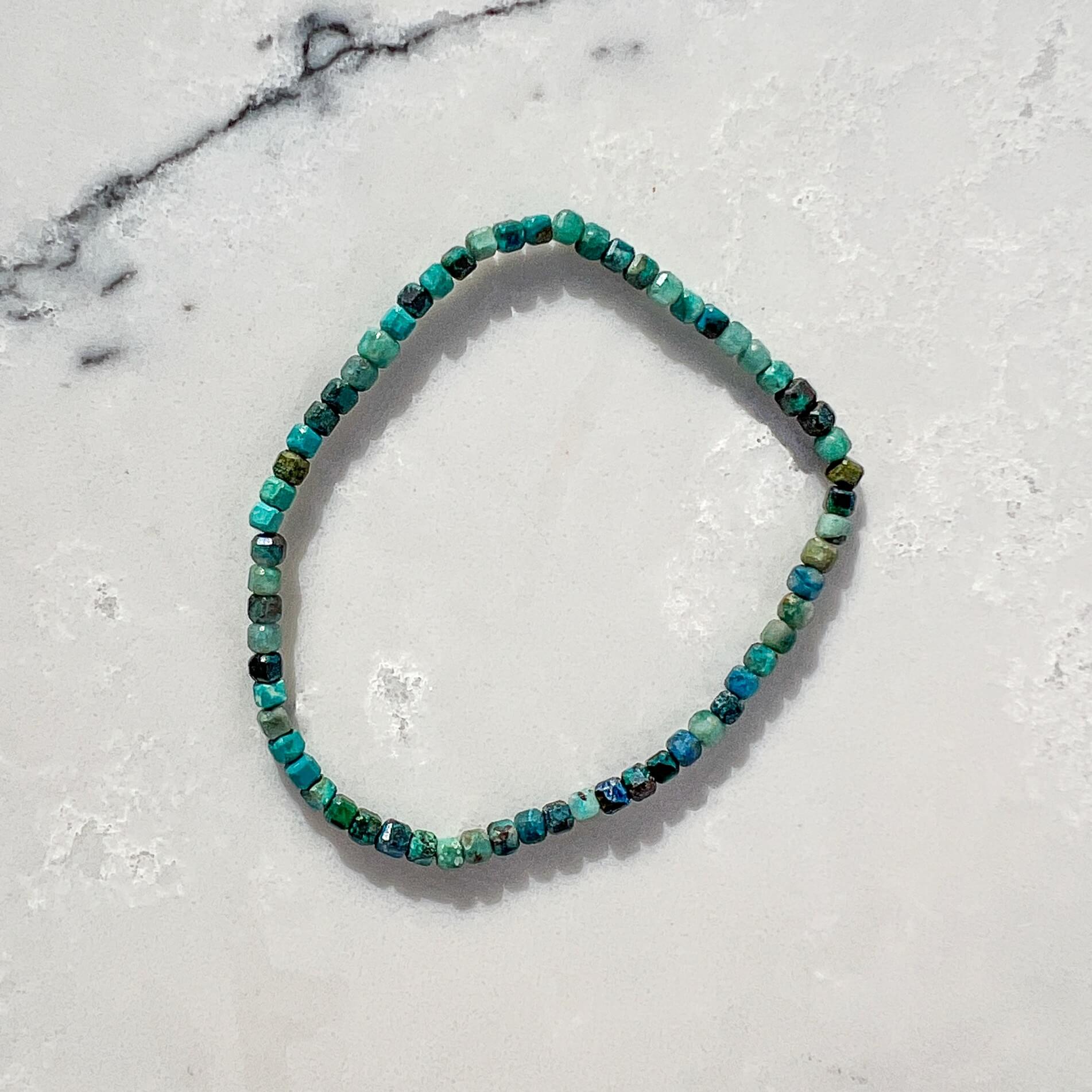 Beaded bracelet with green and teal chrysocolla gemstones on a marble surface