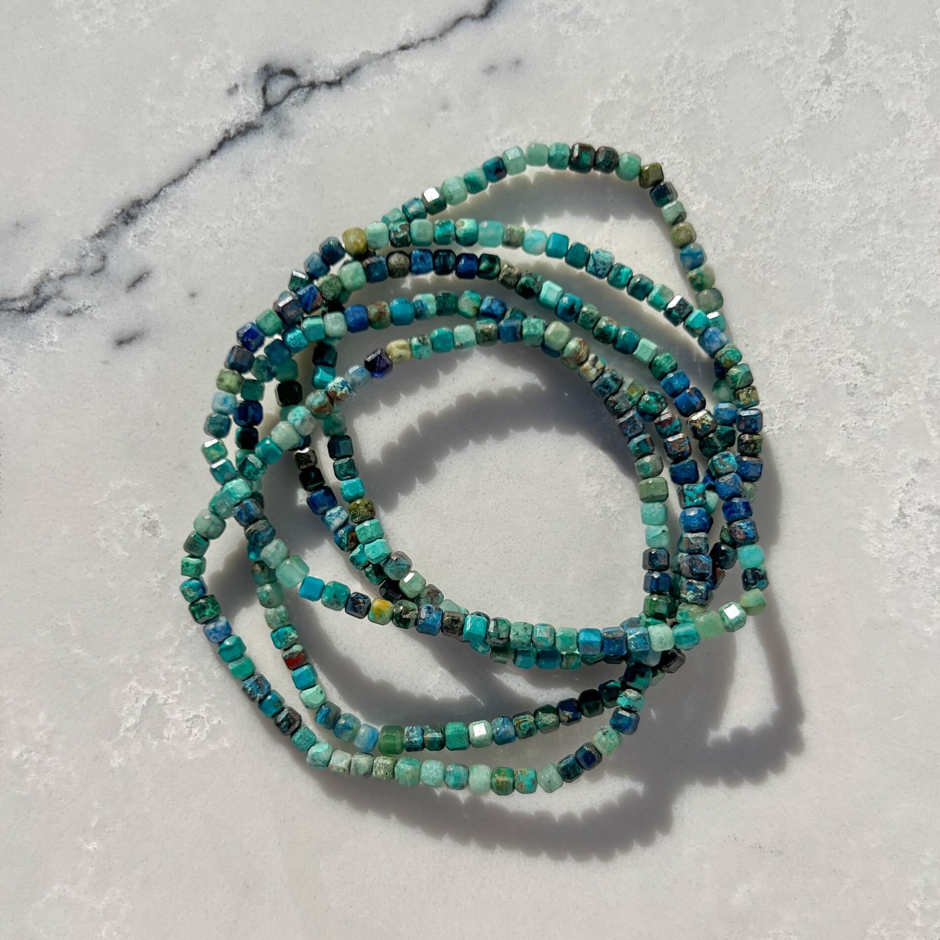 Stack of Chrysocolla crystal Bead bracelets with green and blue stones on a marble surface