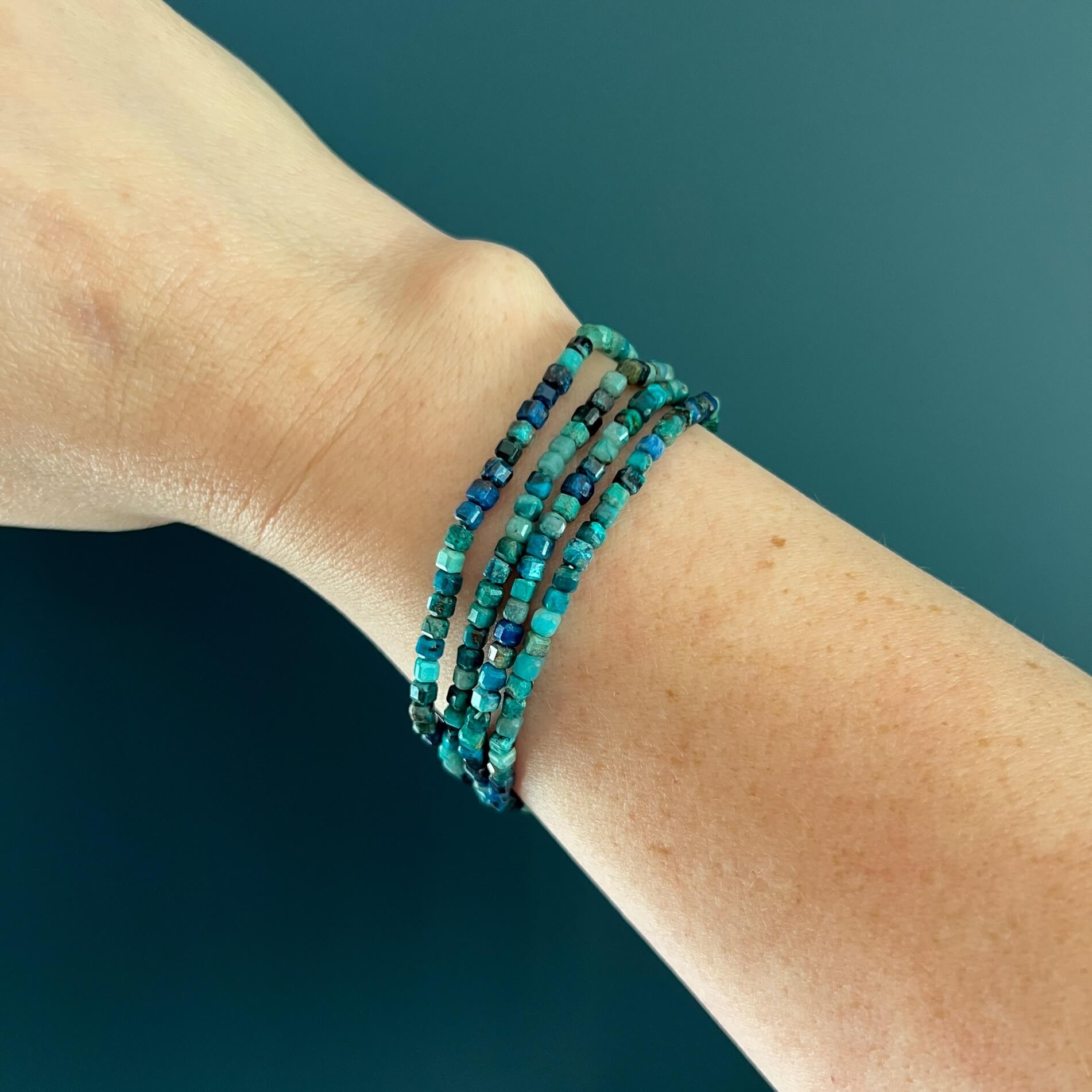 Stack of turquoise chrysocolla bead bracelets on a woman's wrist against a teal background