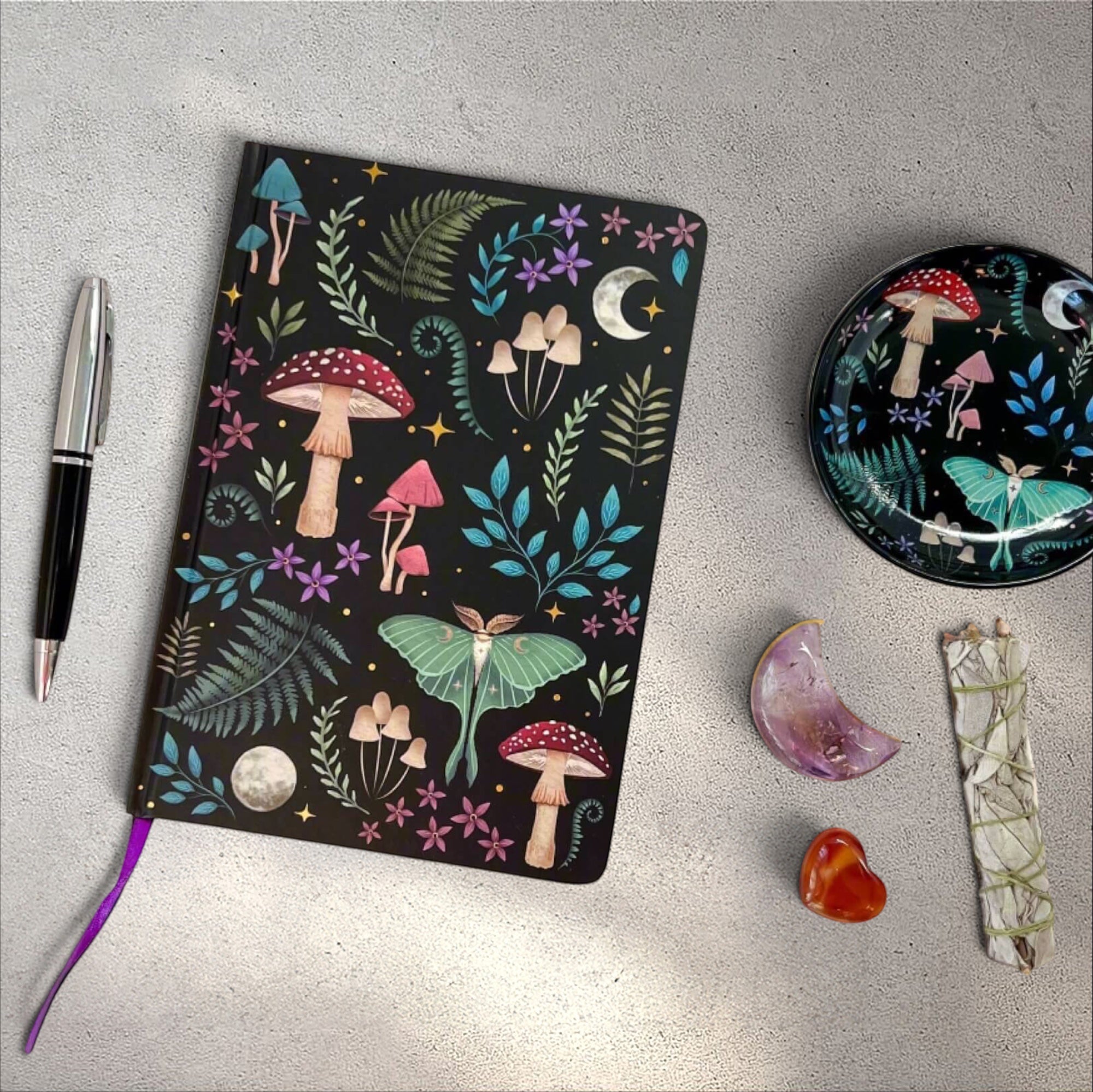 Rock + Realm Crystals Dark Forest A5 notebook with moon, mushrooms, ferns, and luna moth illustration on black cover.
