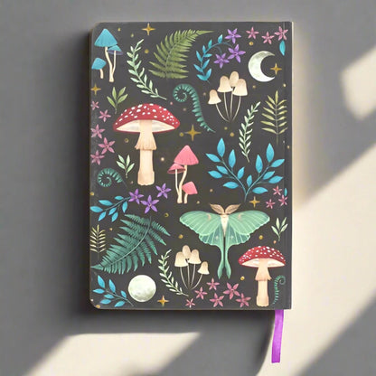 Rock + Realm Crystals Dark Forest A5 notebook with whimsical mushroom, fern, moth, moon, and star illustrations on a dark background.