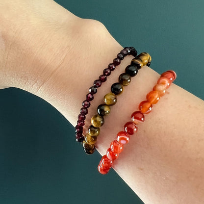Three red crystal bead bracelets on a wrist against a dark teal background