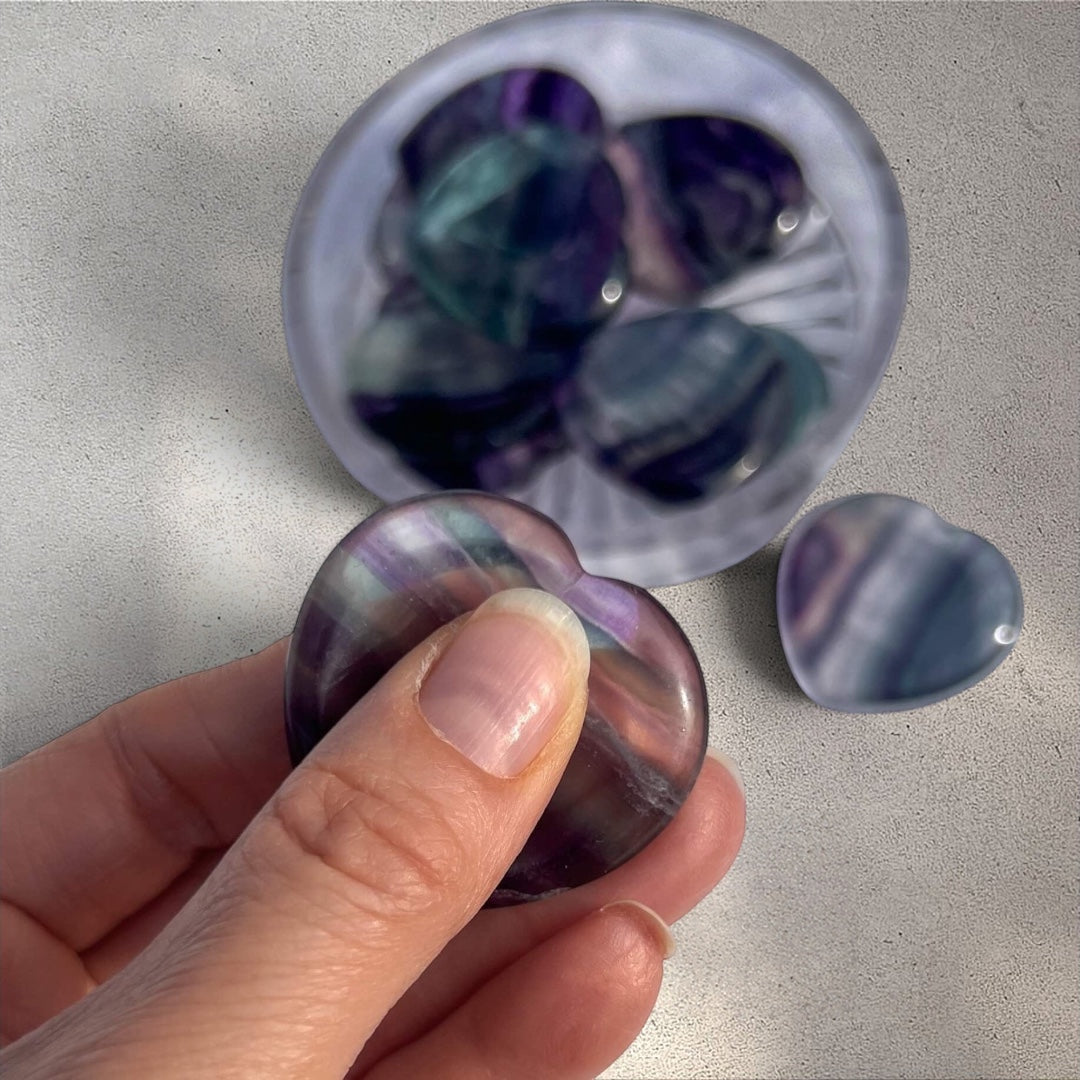 Rock + Realm Crystals blue and purple fluorite heart worry stone, polished smooth with unique banding held between thumb and forefinger
