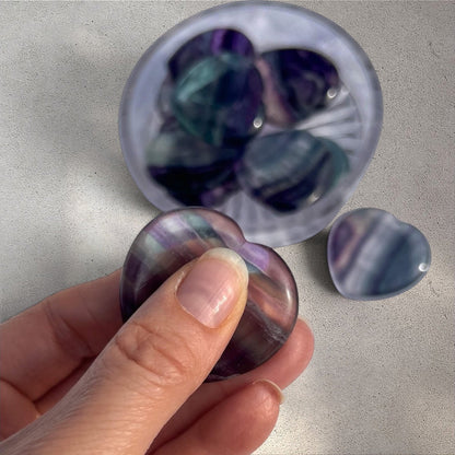 Rock + Realm Crystals blue and purple fluorite heart worry stone, polished smooth with unique banding held between thumb and forefinger