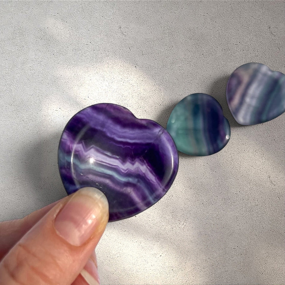 Rock + Realm Crystals blue and purple fluorite heart worry stone with polished surface and distinct  banding pinched by thumb