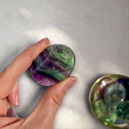 Rock + Realm Crystals polished rainbow fluorite worry stone with purple and green bands, held in hand.