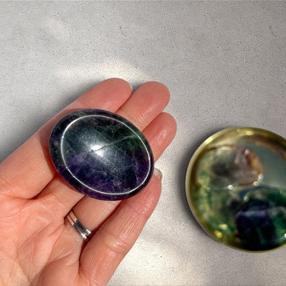 Rock + Realm Crystals polished fluorite worry stone with purple and green bands, held flat on a hand.