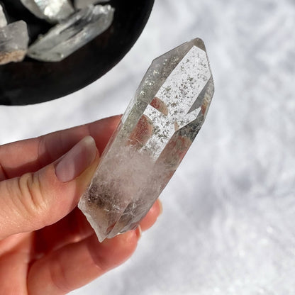 Hand holding a clear garden quartz crystal with a white background