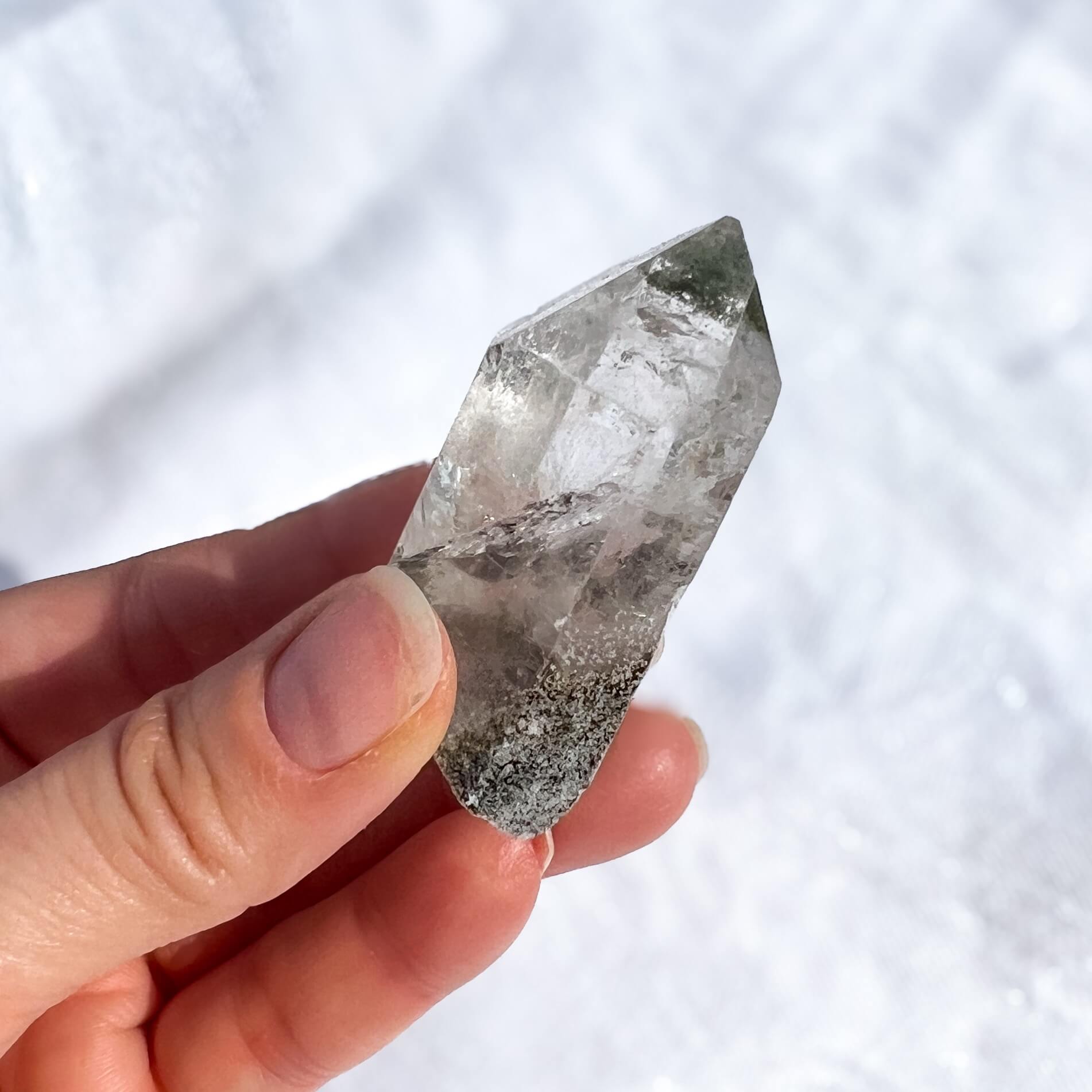 Hand holding a clear garden quartz crystal against a white background