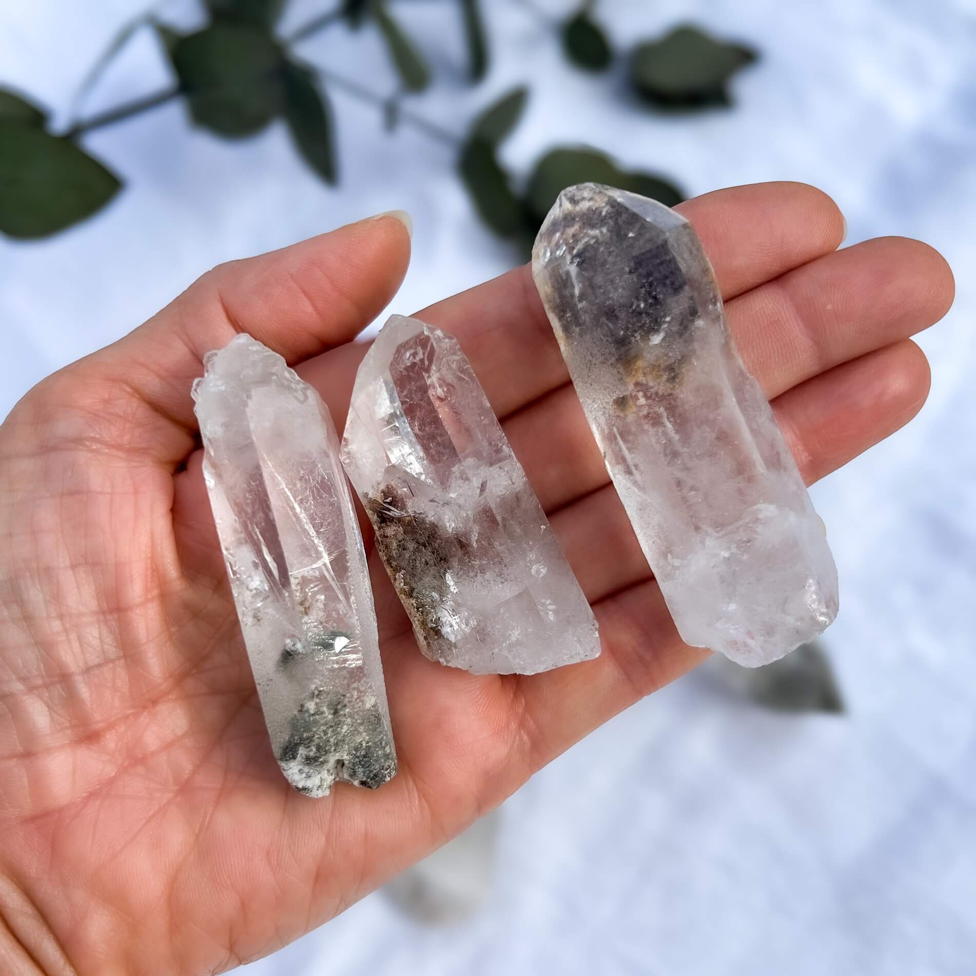 Three crystal points held in a hand with a blurred natural background