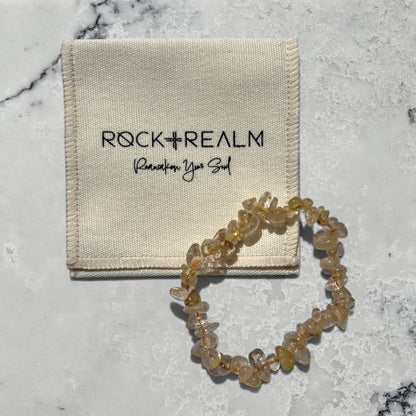 Yellow and clear golden rutilated quartz crystal chip bracelet on a marble surface with cotton 'Rock + Realm' pouch