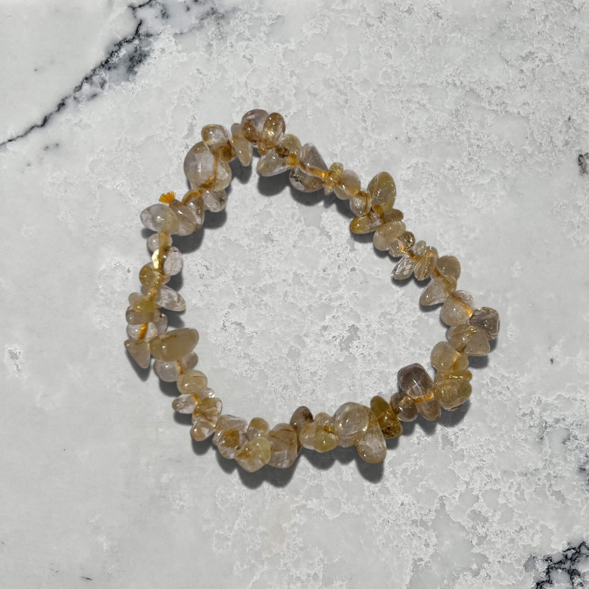 Yellow and clear golden rutilated quartz crystal chip bracelet on a marble surface