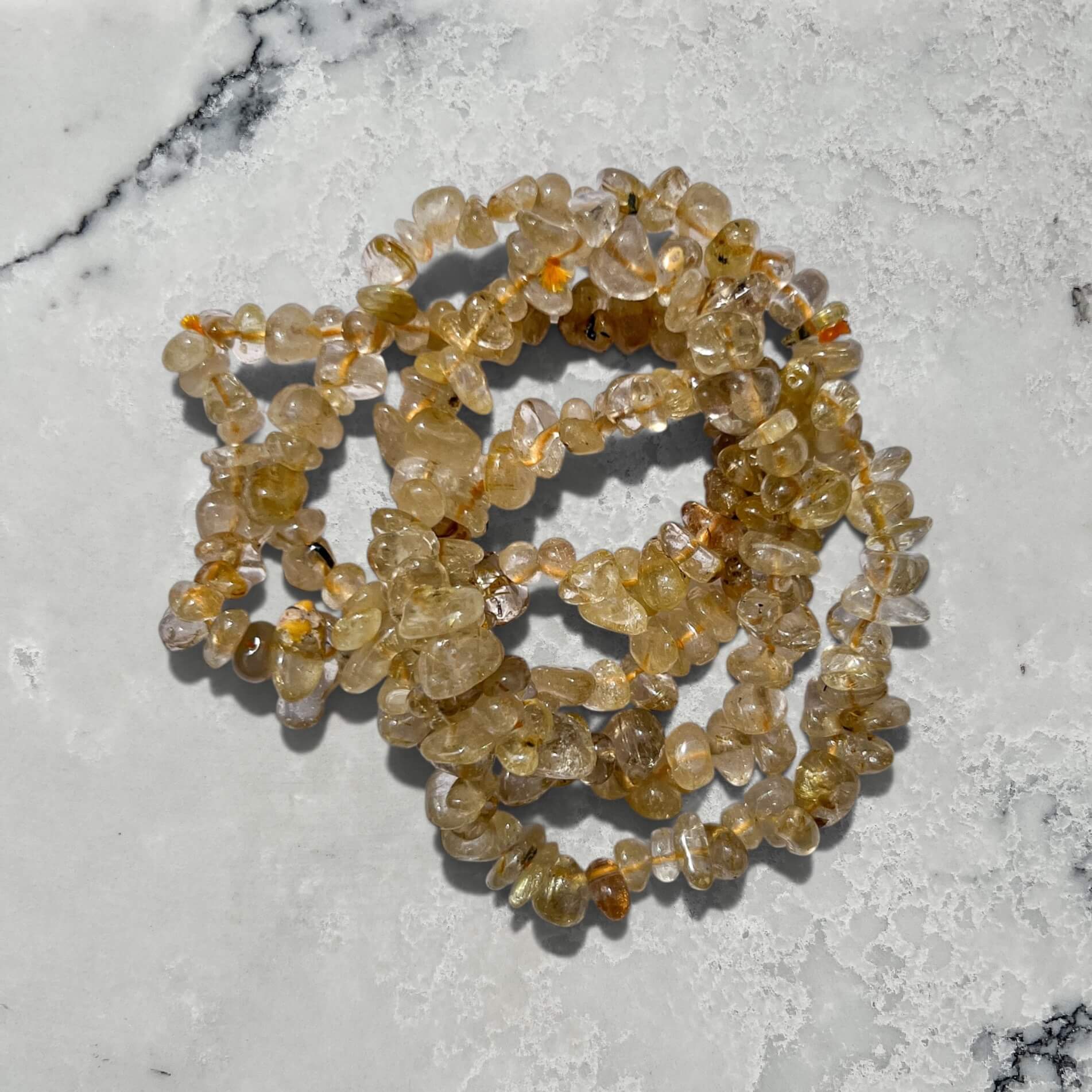 Yellow and clear golden rutilated quartz crystal chip bracelets stacked on a marble surface