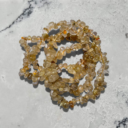 Yellow and clear golden rutilated quartz crystal chip bracelets stacked on a marble surface