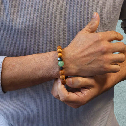 Man in grey top wearing a Cedar wood beaded bracelet with green aventurine and metallic black hematite beads stood against a neutral background