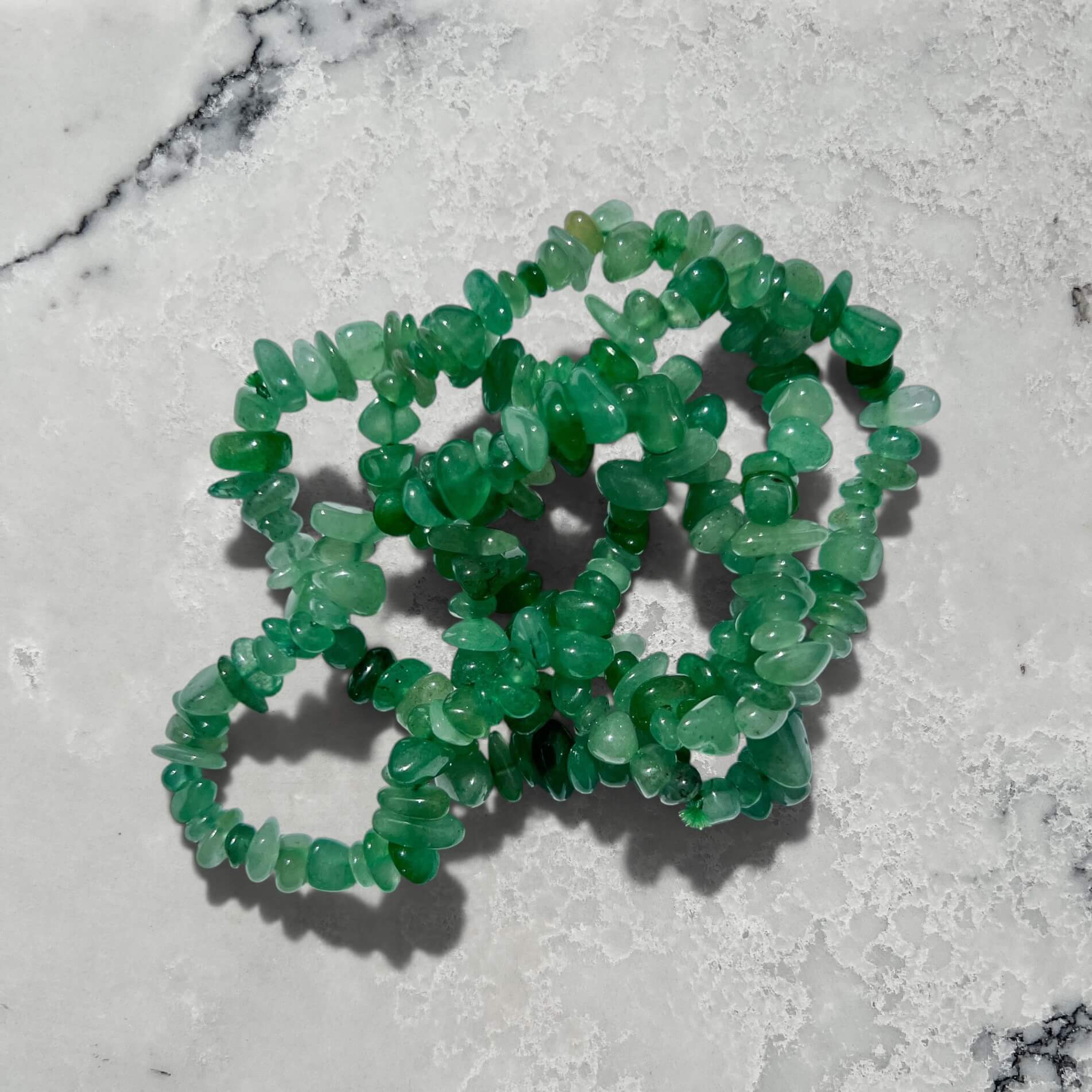 Stack of Green Aventurine crystal chip bracelets on a marble surface