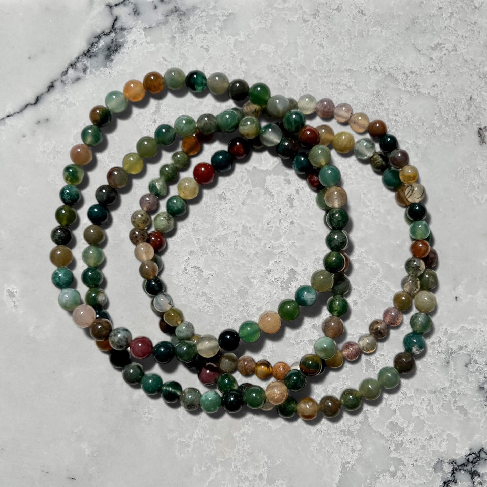 A stack of four Green jasper crystal bead bracelets on a marble surface
