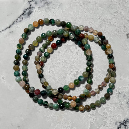 A stack of four Green jasper crystal bead bracelets on a marble surface